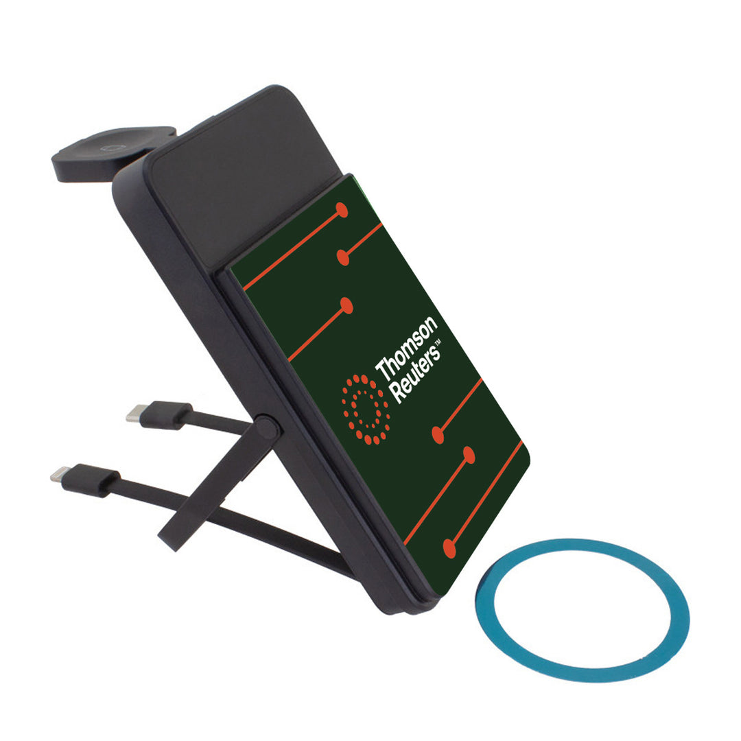 A black 3-in-1 Mag-N Kick power bank with built-in magnets, featuring a dark green front panel with the Thomson Reuters logo in white and orange, two attached charging cables, and a blue metal ring, shown against a plain white background.